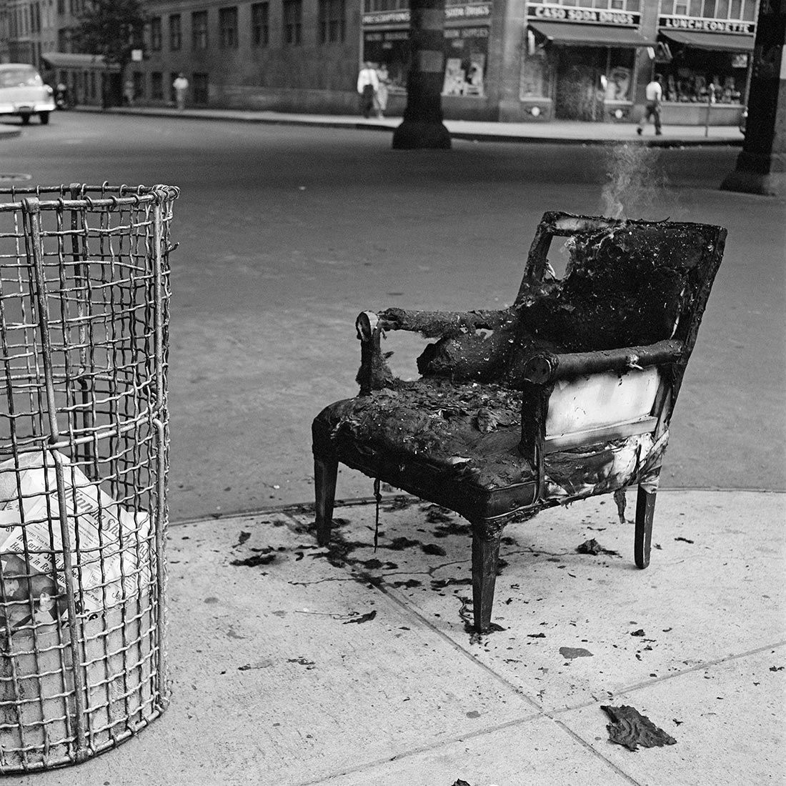 A burnt chair on a street corner with a wisp of smoke rising from it