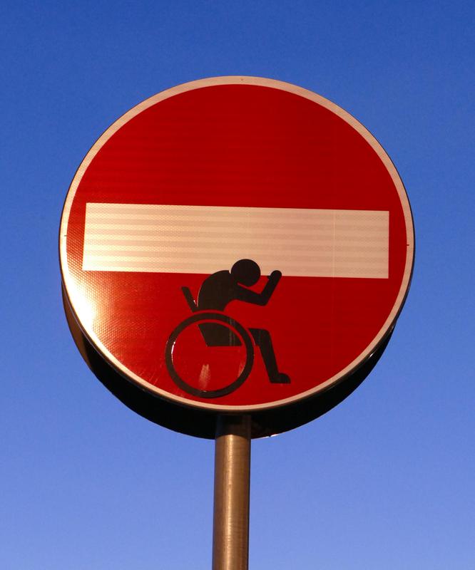 A "no entry" street sign modified to show someone in a wheelchair attempting to support the white no-entry bar