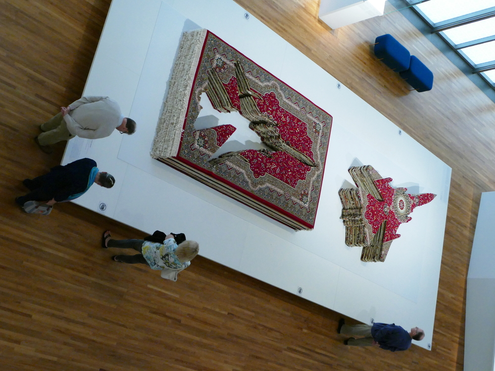 A stack of Persian carpets with the shape of a war plane cut out of them