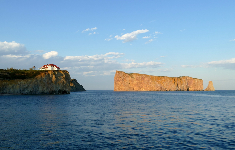 A house on a cliff and the huge Percé Rock with a hole through it