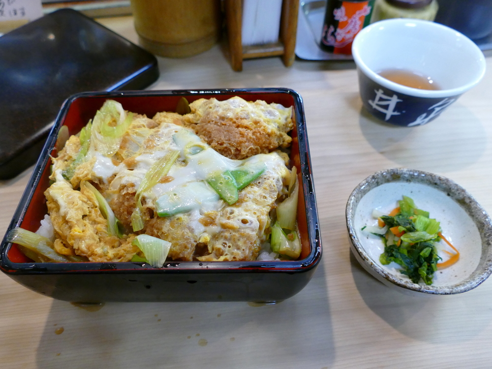 breaded, deep fried pork cutlet with egg on rice, small pickled vegetables on the side