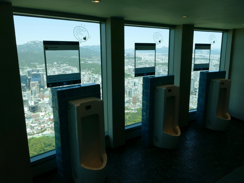 three urinals with big picture windows in front of them with one hell of a view of Seoul