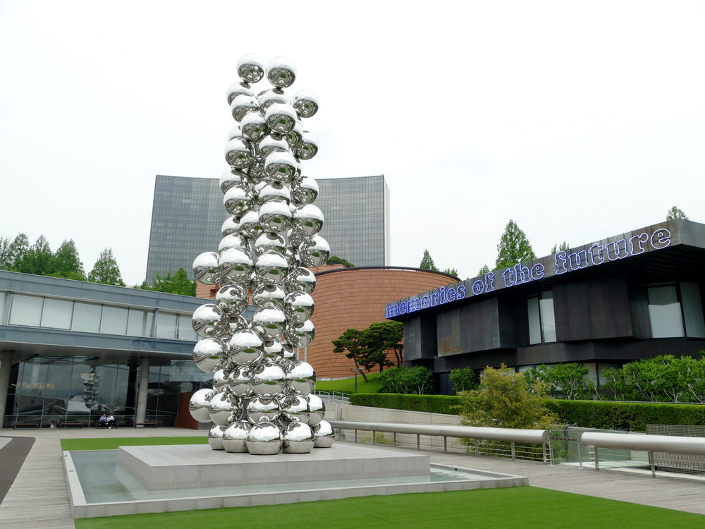 three diverse buildings with a sculpture of a heap of reflective spheres in front