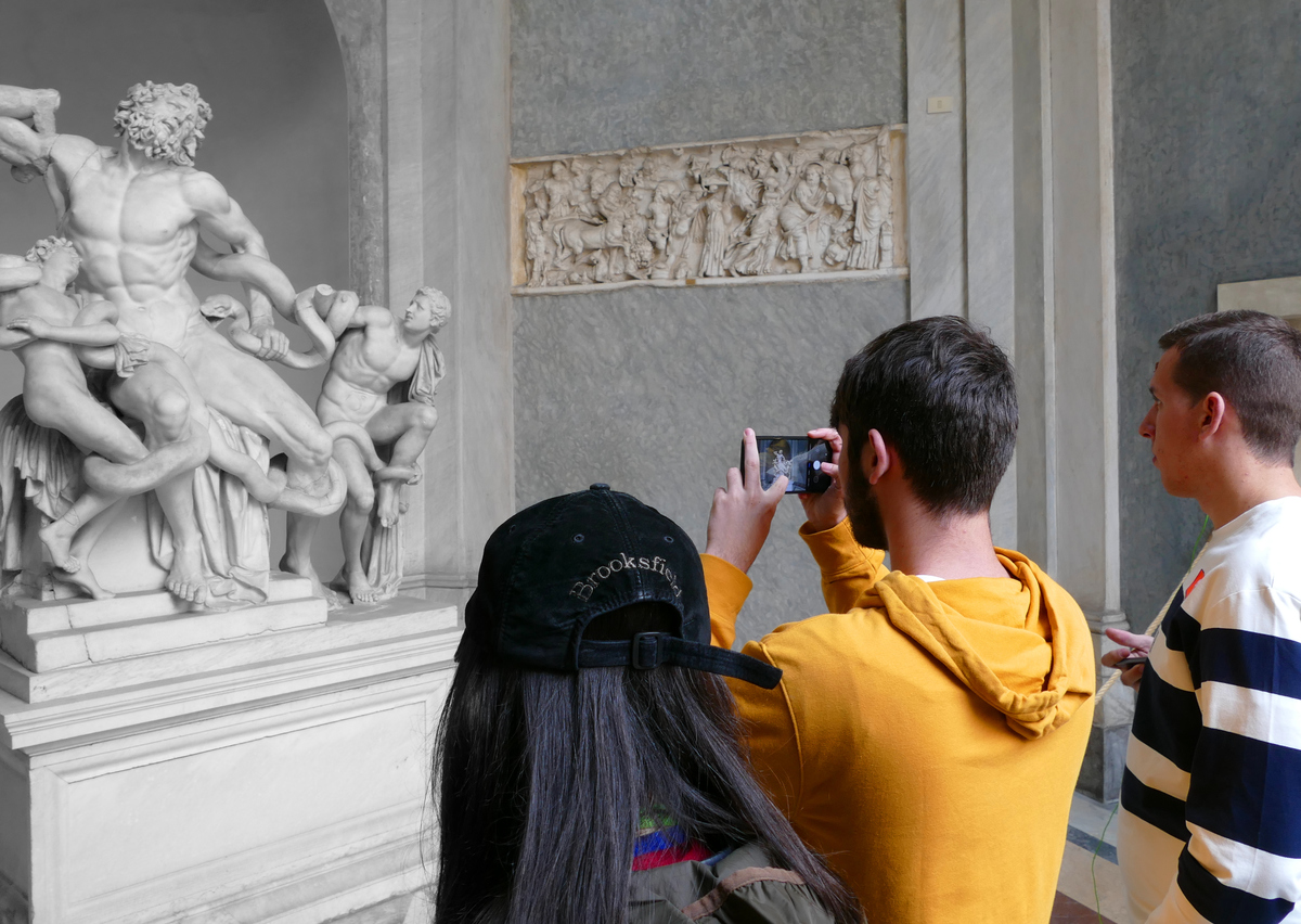 marble sculpture being viewed by teens, one taking pictures with his phone