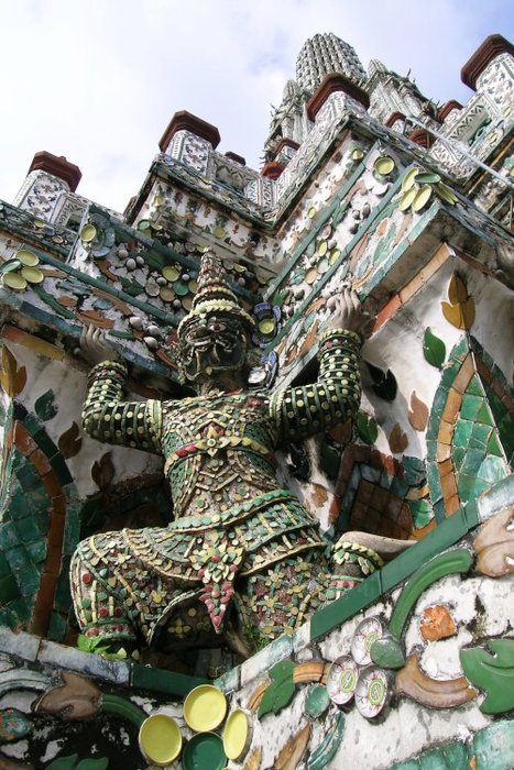 Demon sculpture holding up the towering pottery-plated Wat Arun