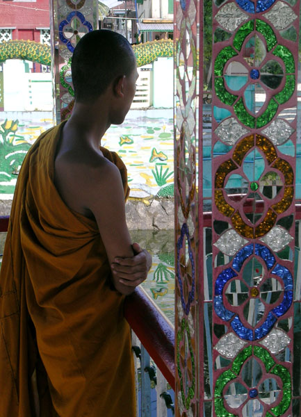 a Buddhist monk in an orange robe looking out between mirror-tiled columns