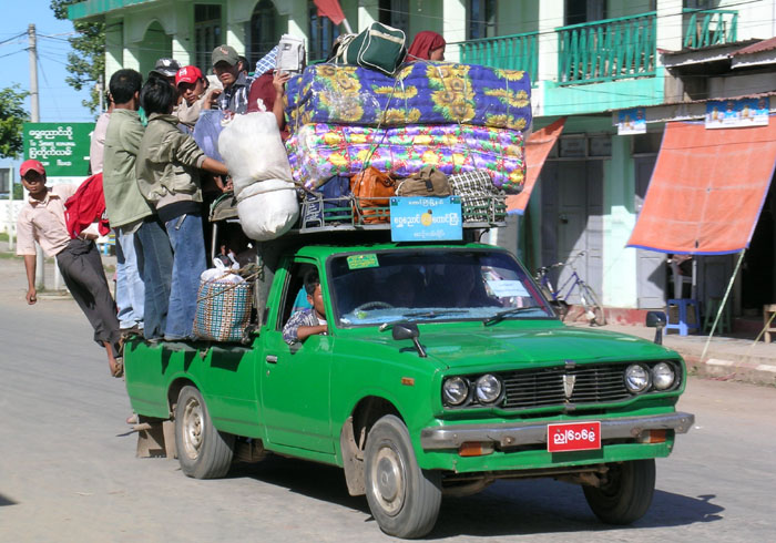 a small green pick-up truck with about 35 people and luggage on it