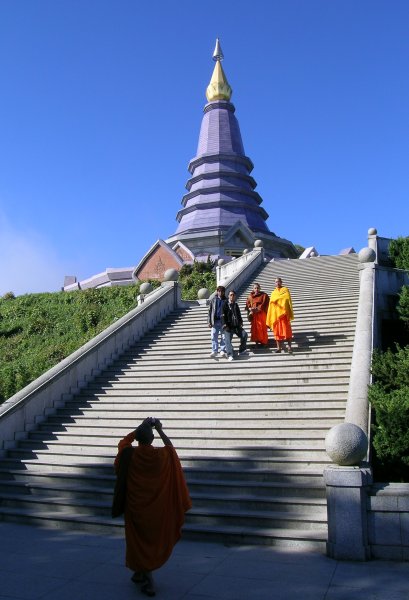 A monk with a digital camera takes a photo of two monks and two friends in front of a stupa.