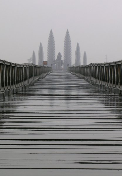 A long wood-planked bridge in the rain, with a menacing monument at the end.