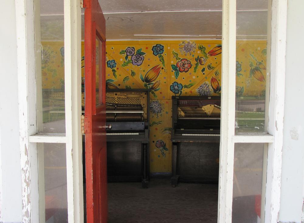 looking through a door at two decrepit pianos