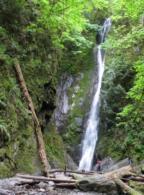Very tall falls in Goldstream Provincial Park with a couple people in front of it.