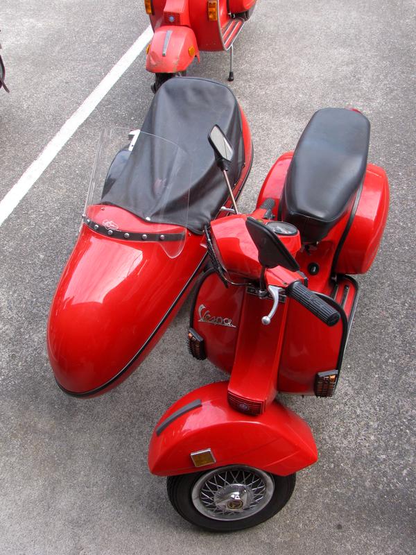 A bright red Vespa scooter with sidecar
