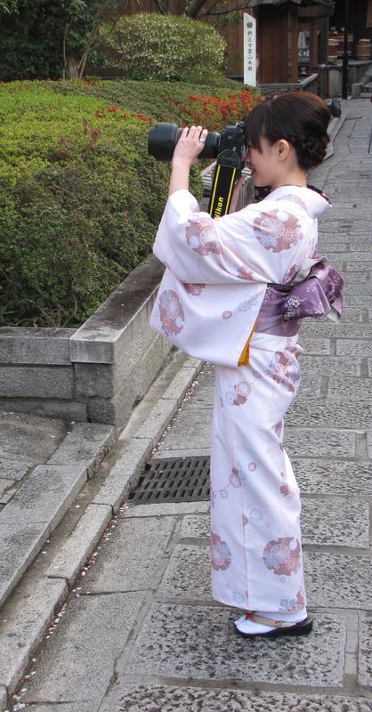 A woman in a kimono focuses her very large camera